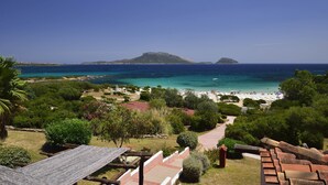 A coastal view with a beach, clear blue sea, and a mountain in the distance. - VOI Colonna Village (Golfo Aranci)