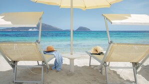 Two beach chairs with a large umbrella, a small table, and a book on one of the chairs. - VOI Colonna Village (Golfo Aranci)
