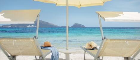 Two beach chairs with a large umbrella, a small table, and a book on one of the chairs.