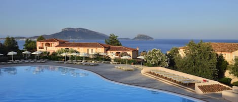 A swimming pool with lounge chairs and umbrellas, a building with a tiled roof, and a view of the sea and distant islands.