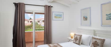 Ein Schlafzimmer mit Bett, Vorhängen, einem Nachttisch und einem Balkon.