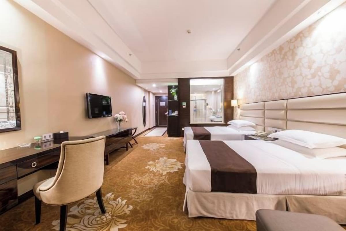 A hotel room with two beds, a desk, a chair, and a television.