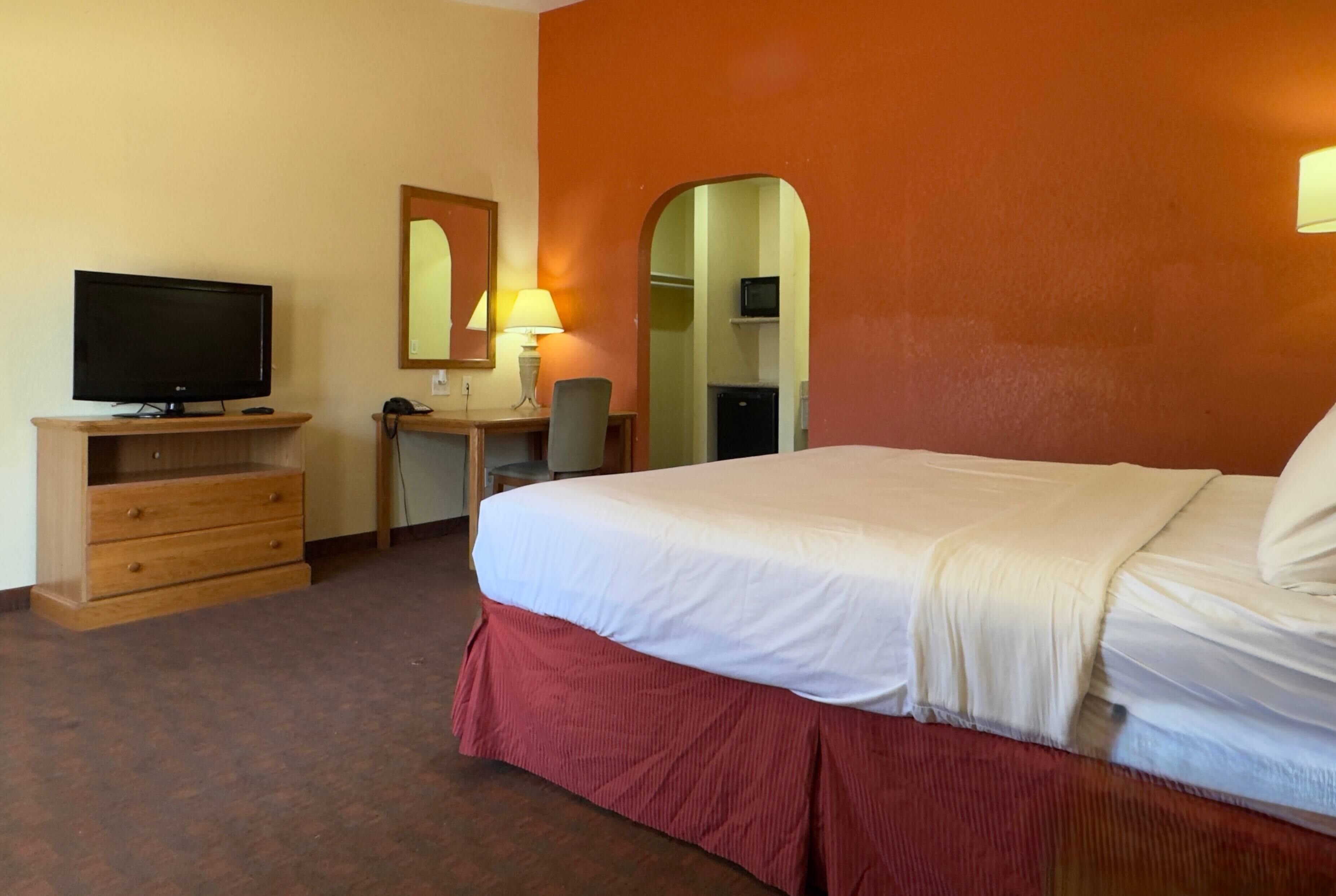 A hotel room with a bed, a desk with a computer, a television, and a mirror.