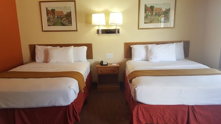A hotel room with two beds, each with white linens and red bedspreads. There are two wall-mounted lamps above the beds, and two framed pictures on the wall.