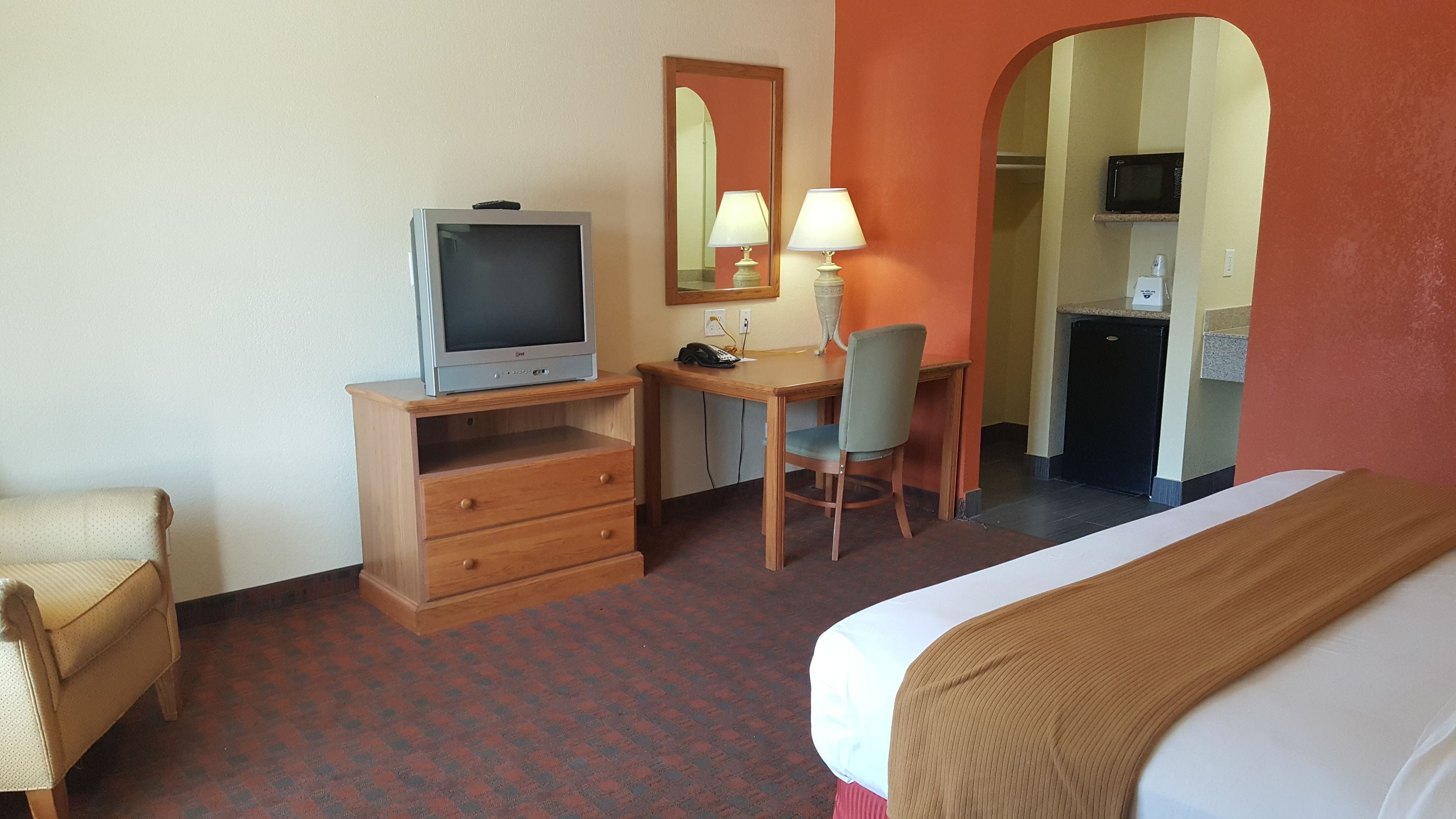 A hotel room with a bed, a desk with a chair, a television, a lamp, and a microwave.
