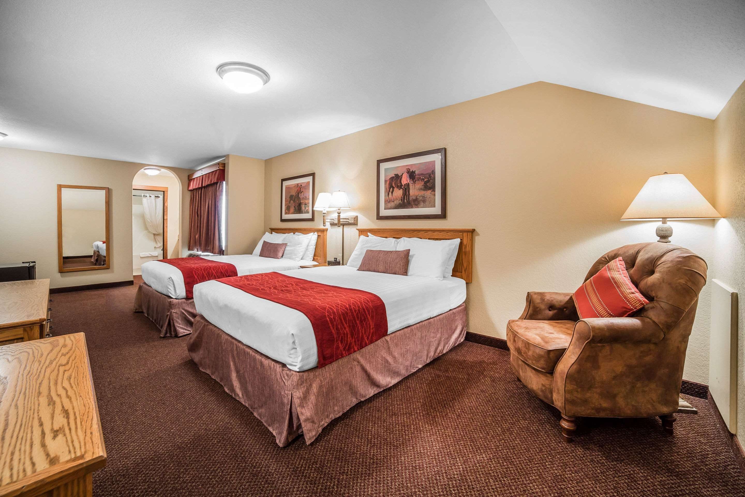 A hotel room with two beds, a chair, a desk, and a mirror.
