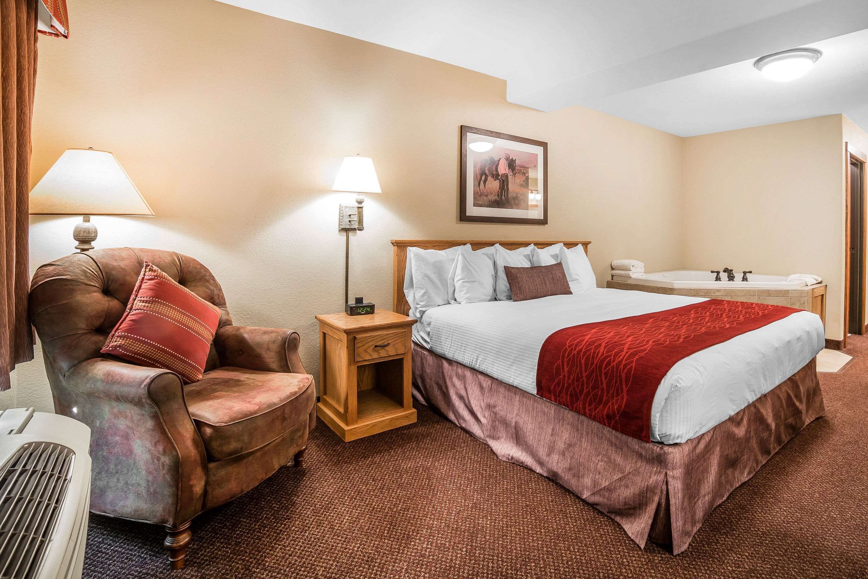 Una camera d'albergo con un letto grande, una sedia, un comodino, una lampada e un quadro appeso al muro.