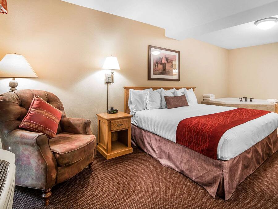 Una camera d'albergo con un letto grande, una sedia, un comodino, una lampada e un quadro appeso al muro.
