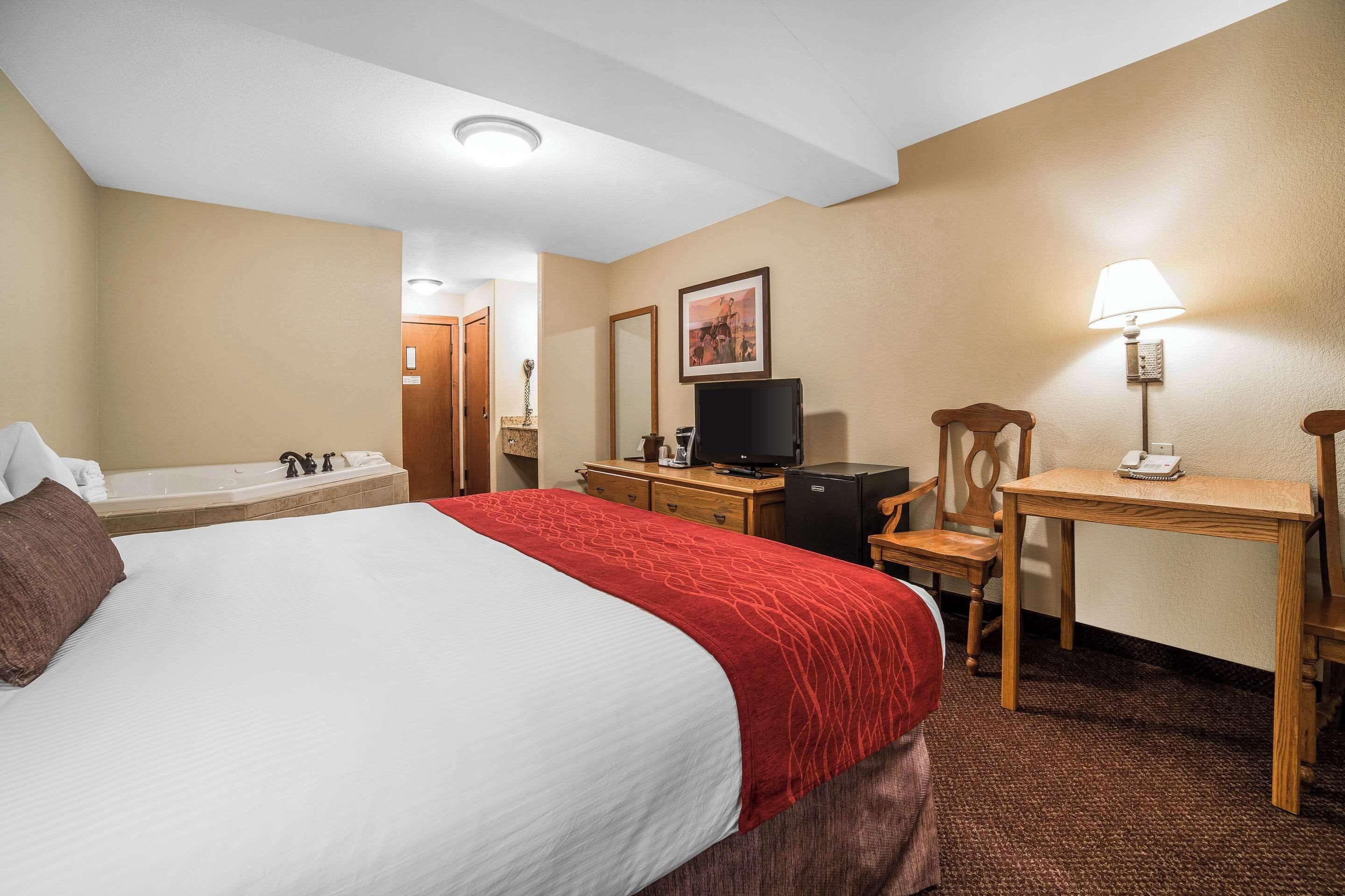 Une chambre d’hôtel comprenant un grand lit, un bureau, une chaise, une télévision, une lampe, ainsi qu’une salle de bain avec une baignoire et un lavabo.