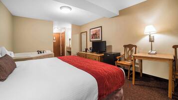 Une chambre d’hôtel comprenant un grand lit, un bureau, une chaise, une télévision, une lampe, ainsi qu’une salle de bain avec une baignoire et un lavabo.