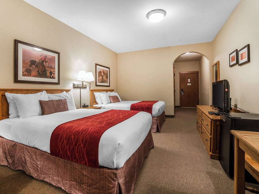 A hotel room with two beds, a desk, a TV, and a door leading to another room.