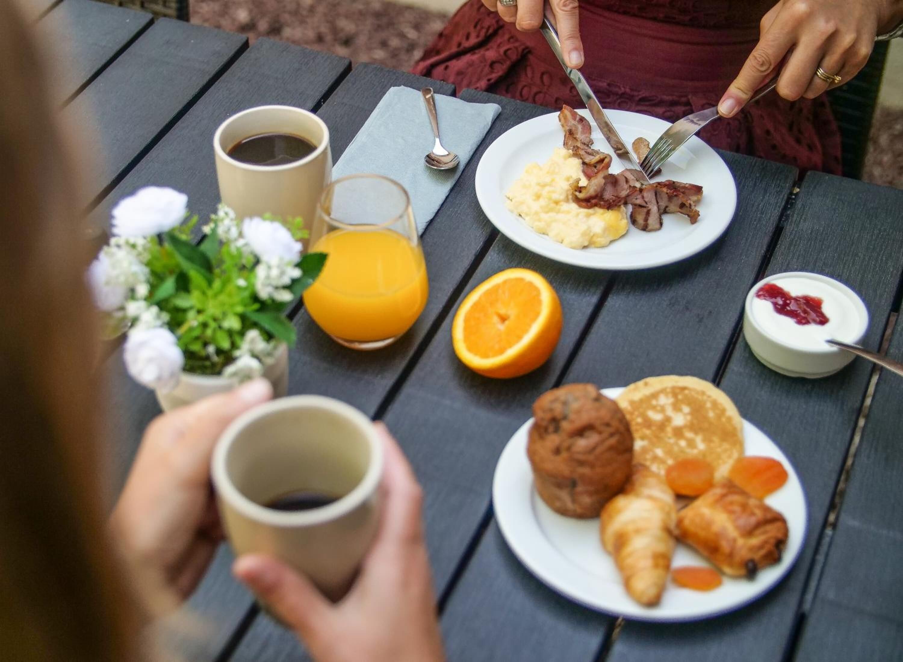 A breakfast setting with a plate of scrambled eggs, bacon, orange juice, and pastries on a wooden table.