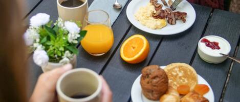 A breakfast setting with a plate of scrambled eggs, bacon, orange juice, and pastries on a wooden table.