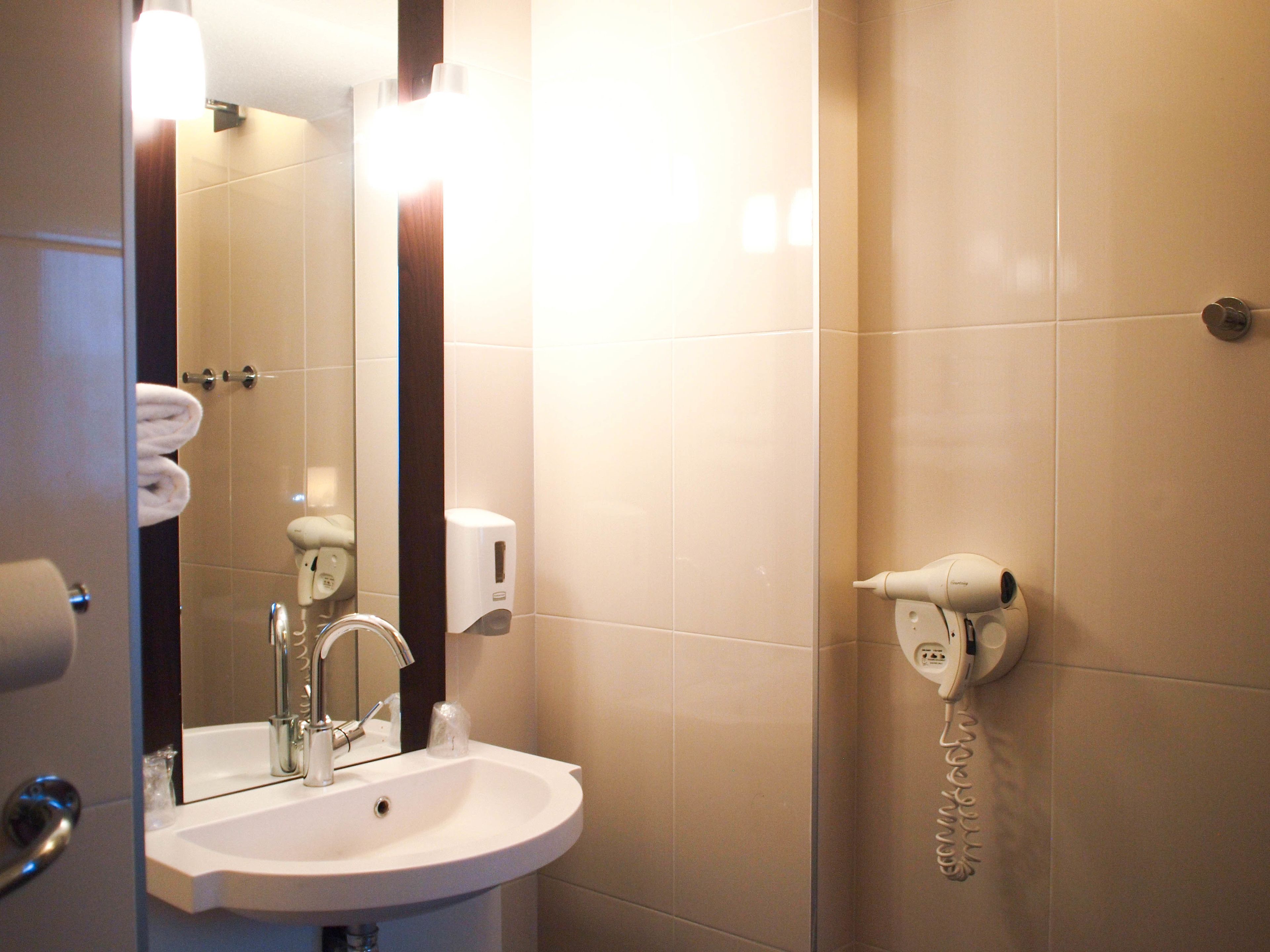 A bathroom with a sink, mirror, towel rack, soap dispenser, and a hairdryer on a wall.