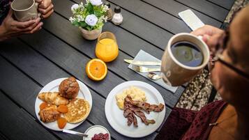 A breakfast setting with plates of food, a coffee mug, and a glass of orange juice on a wooden table.