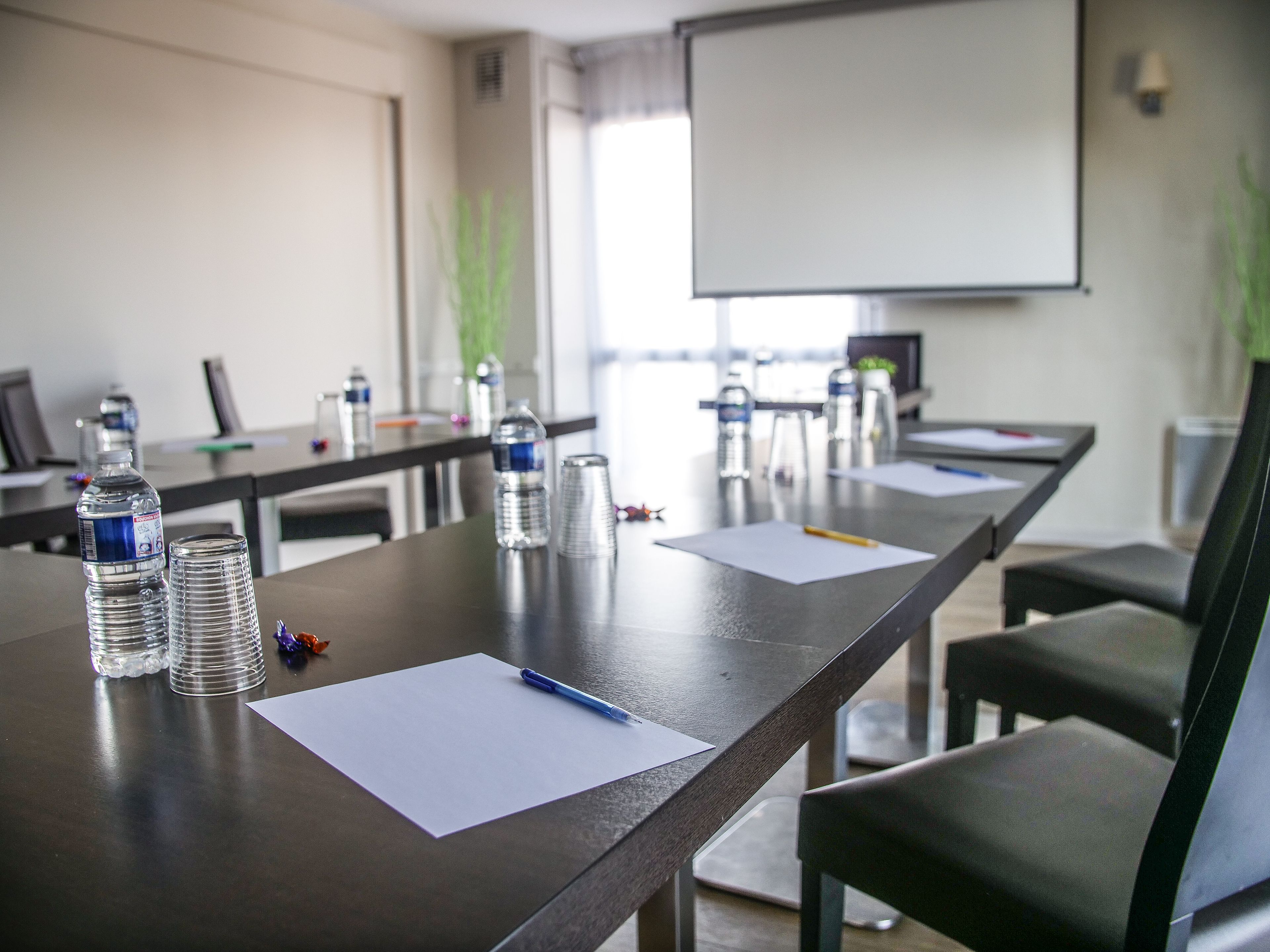 Sala de conferências com uma mesa comprida, garrafas de água, papéis e canetas.