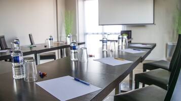 Sala de conferências com uma mesa comprida, garrafas de água, papéis e canetas.