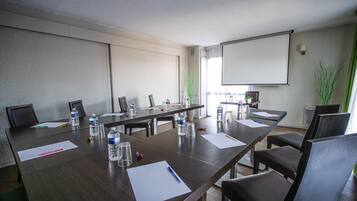 Una sala de conferencias con una larga mesa, sillas, botellas de agua, documentos y una pantalla de proyector.