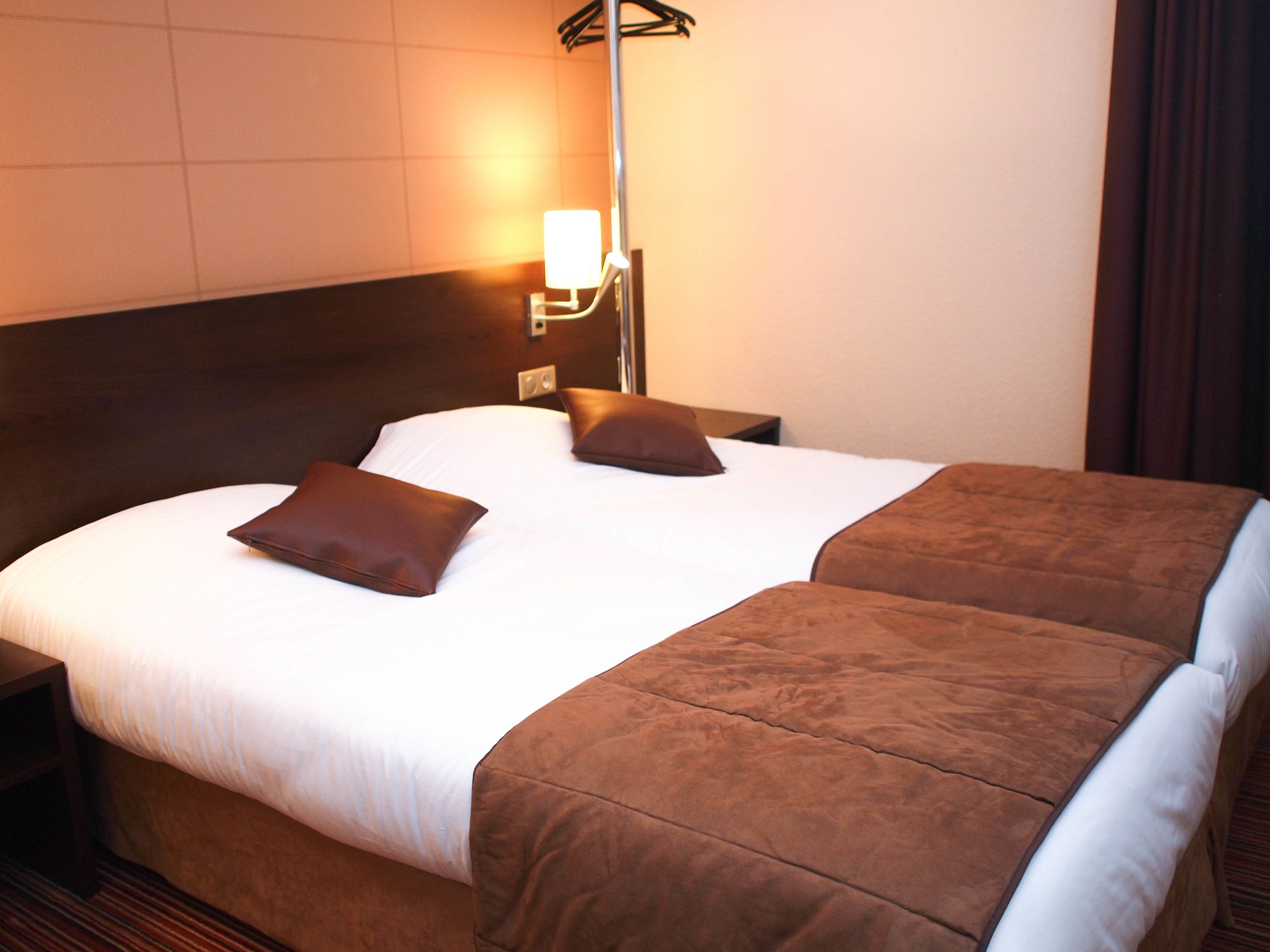 A neatly made double bed with two pillows, a bedside table, and a wall-mounted lamp.
