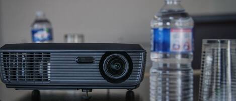 A projector on a table with a water bottle and glasses in the background.