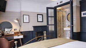 A bedroom with a bed, a desk, a chair, a fireplace, and a bathroom with a sink and mirror. - The Swan Hotel (Staines)