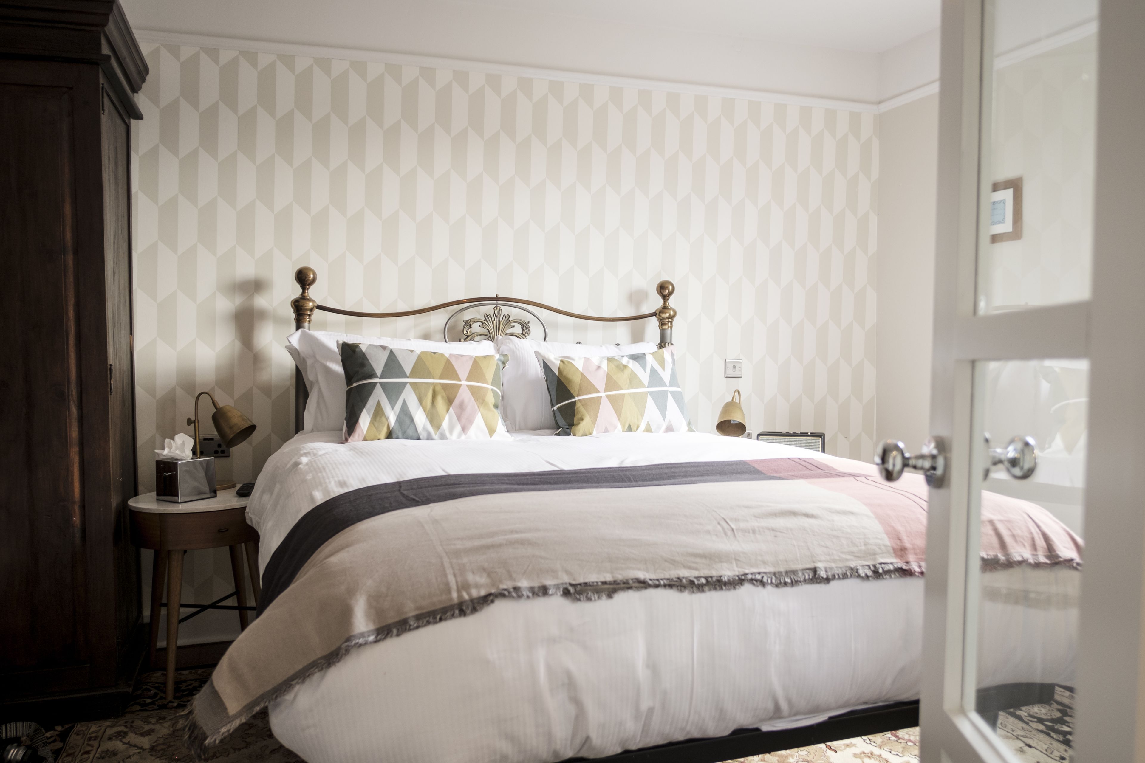 A neatly made bed with a patterned headboard, a bedside table with a lamp, and a door to the right.