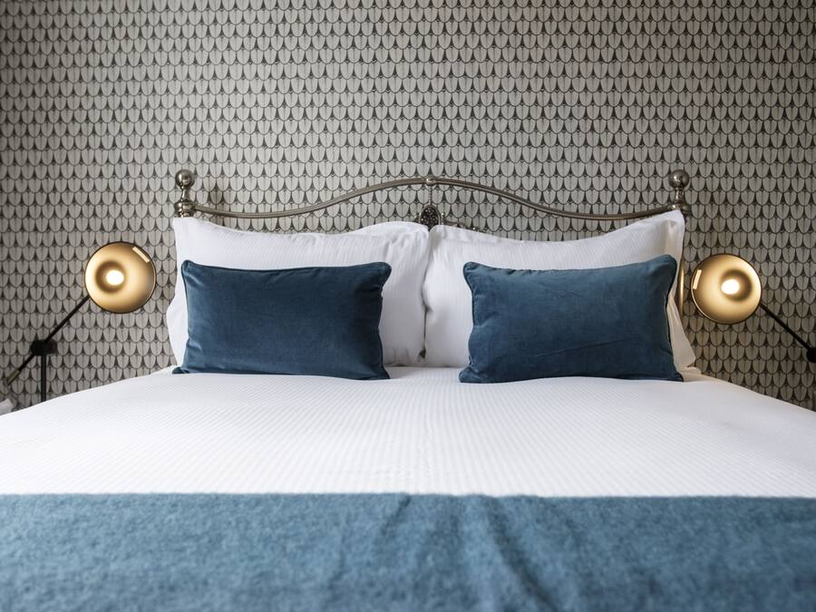 A neatly made bed with a patterned wallpaper background, two bedside lamps, and a blue throw blanket.