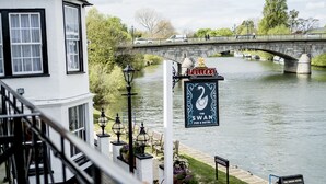 A riverside pub named 'The Swan' with a swan sign, outdoor seating, and a stone bridge in the background. - The Swan Hotel (Staines)