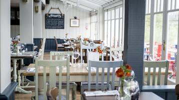 A restaurant interior with wooden tables and chairs, clear glassware, and a chalkboard menu.