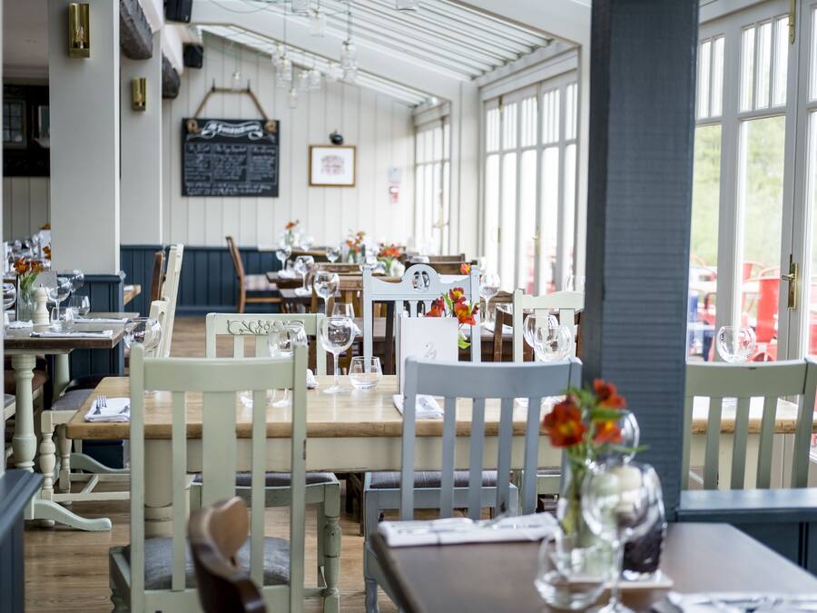 A restaurant interior with wooden tables and chairs, clear glassware, and a chalkboard menu.