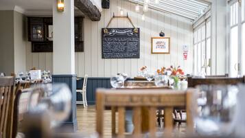 A restaurant interior with wooden tables, chairs, a chalkboard menu, and large windows.