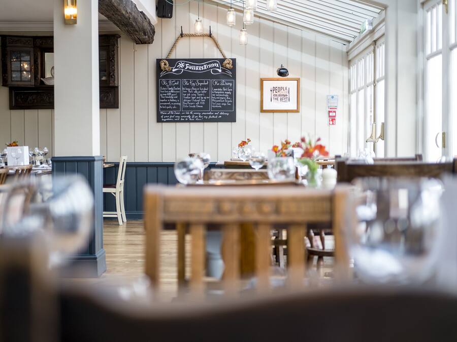 A restaurant interior with wooden tables, chairs, a chalkboard menu, and large windows.