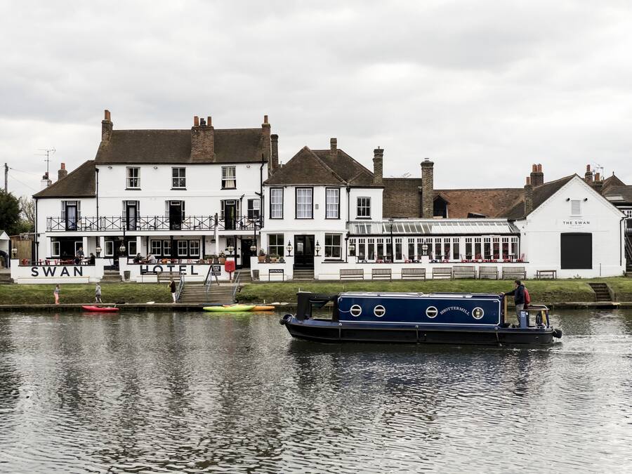 A traditional white building with a sign reading "Swan Hotel" and a boat docked in front.