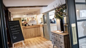A reception area with a wooden counter, a blackboard with text, and a vase of flowers. - The Swan Hotel (Staines)