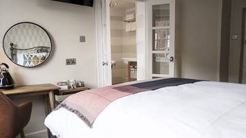 A bedroom with a bed, a desk with a chair, a mirror, and an open door leading to a bathroom.