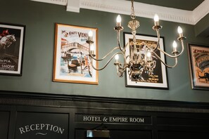 A reception area with a chandelier, framed posters, and a sign for the Hotel & Empire Room.
