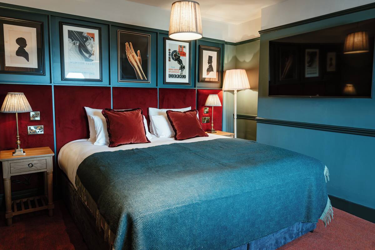 Quarto de hotel com uma cama grande, cabeceira vermelha e várias imagens emolduradas na parede.