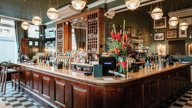 A bar with a checkered floor, wooden counter, and hanging lights. - Hand & Flower (London)