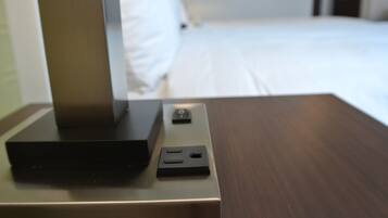 A hotel room with a bed, a bedside table with a television and a power outlet.