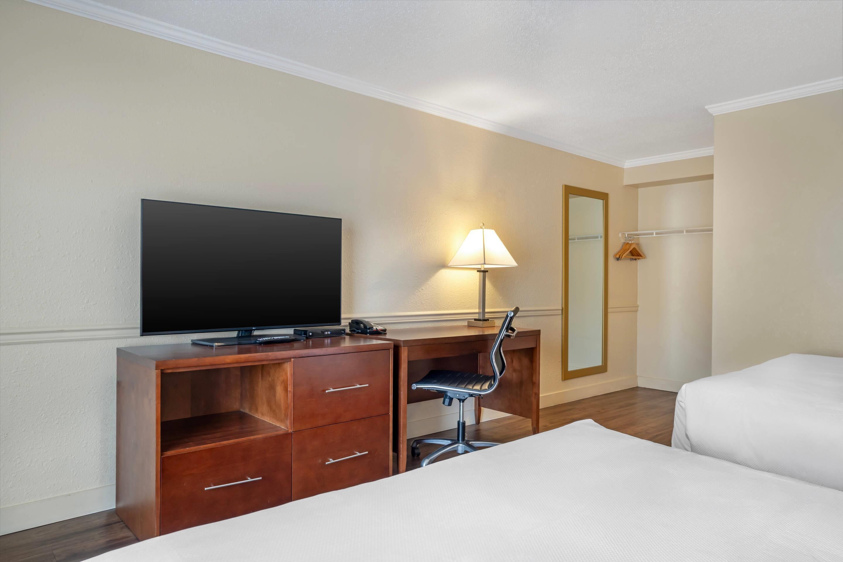 A hotel room with a bed, a desk with a TV, a lamp, and a mirror.