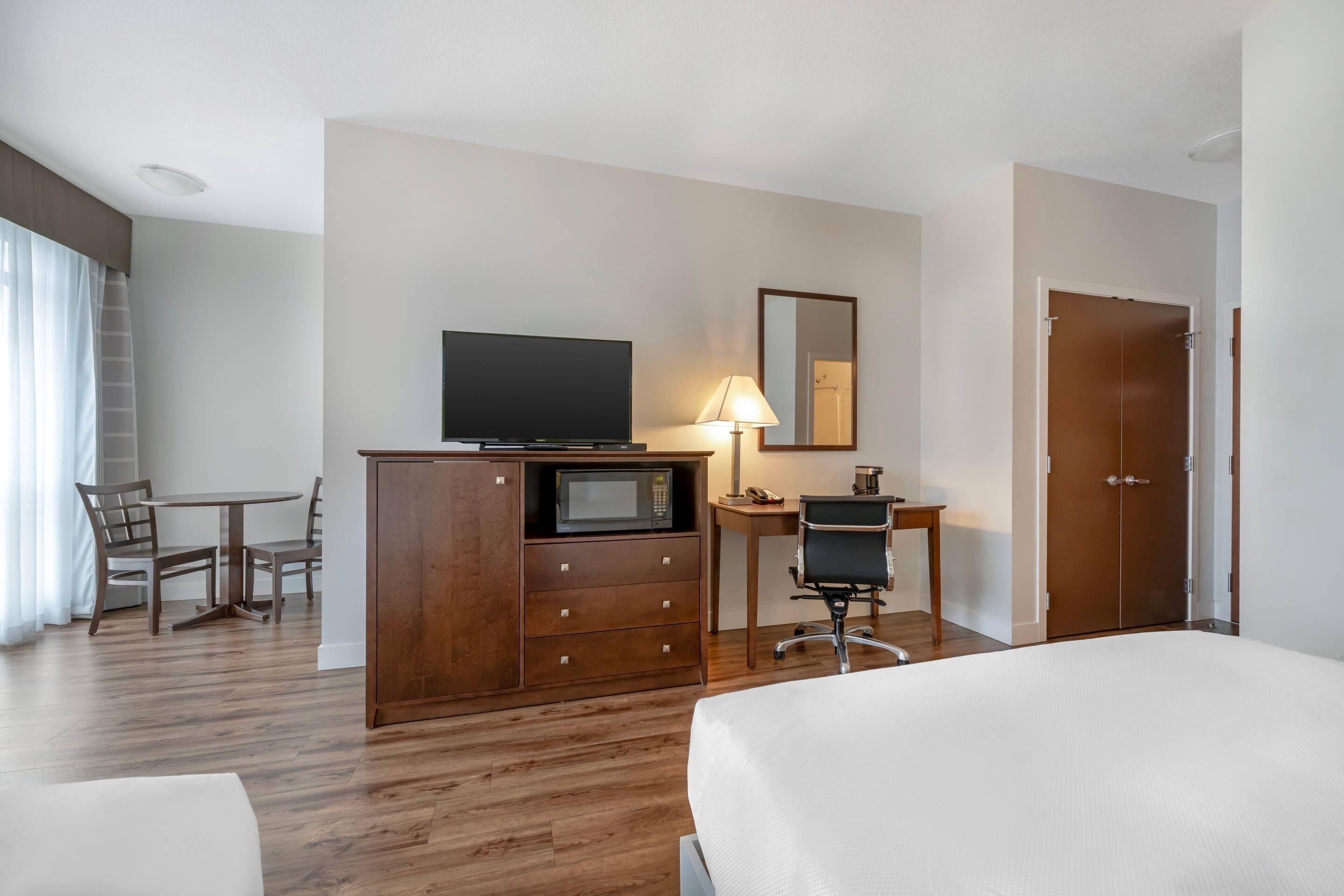 Habitación de hotel con cama, escritorio con computadora, televisión, microondas y armario.