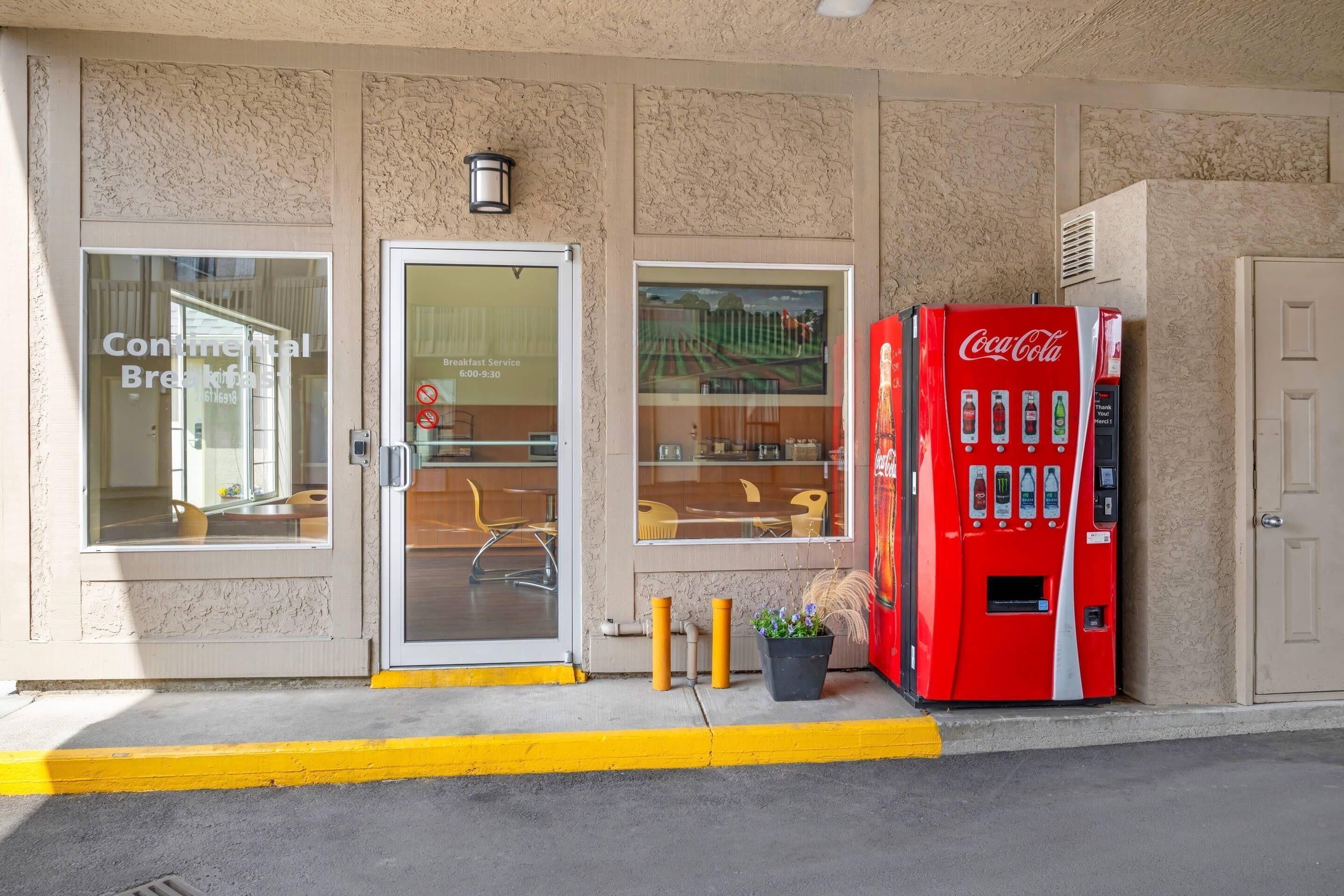 L’entrée d’un hôtel, avec un distributeur automatique de Coca-Cola, une porte vitrée et une fenêtre donnant sur l’intérieur.