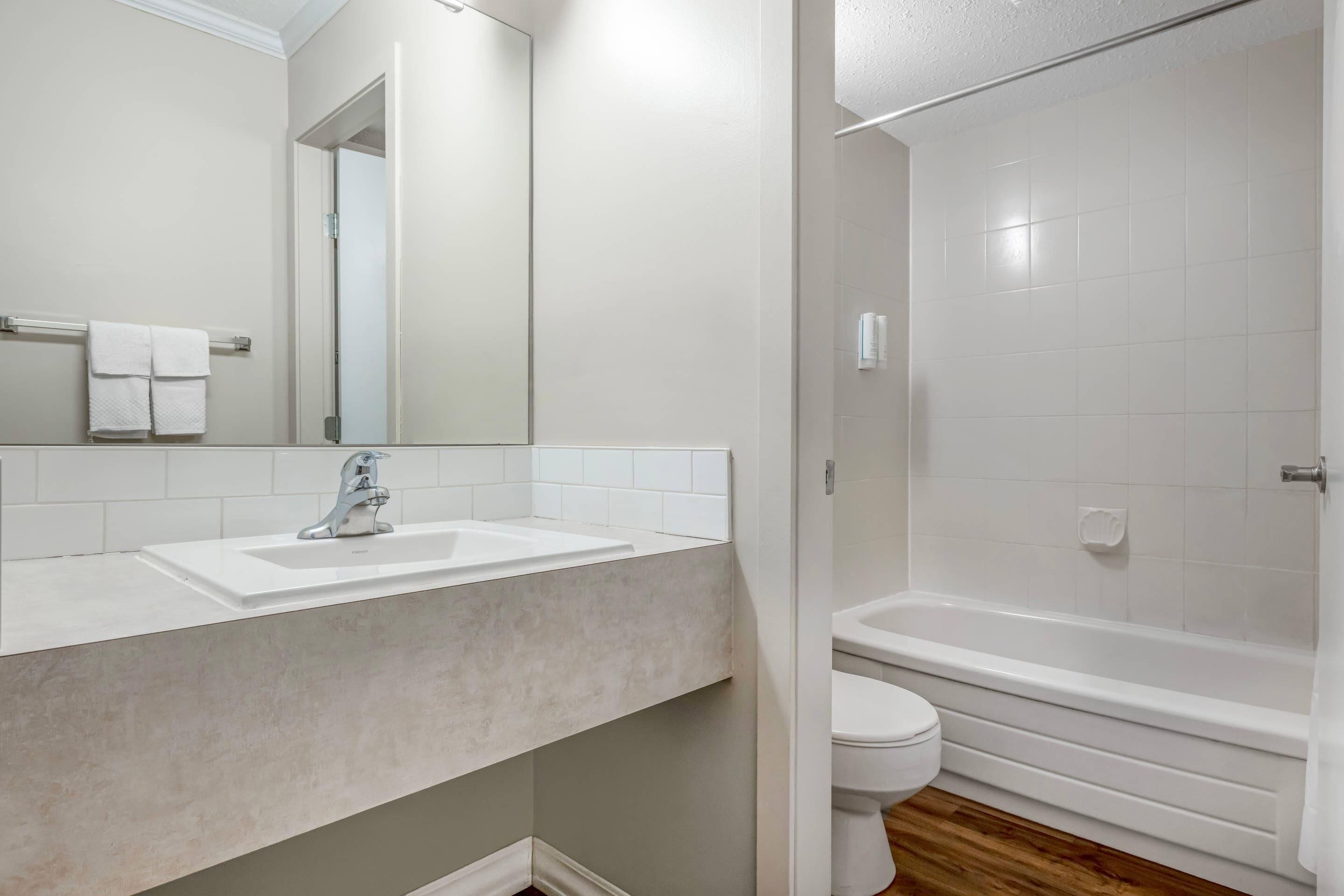 A bathroom with a sink, mirror, toilet, and bathtub.