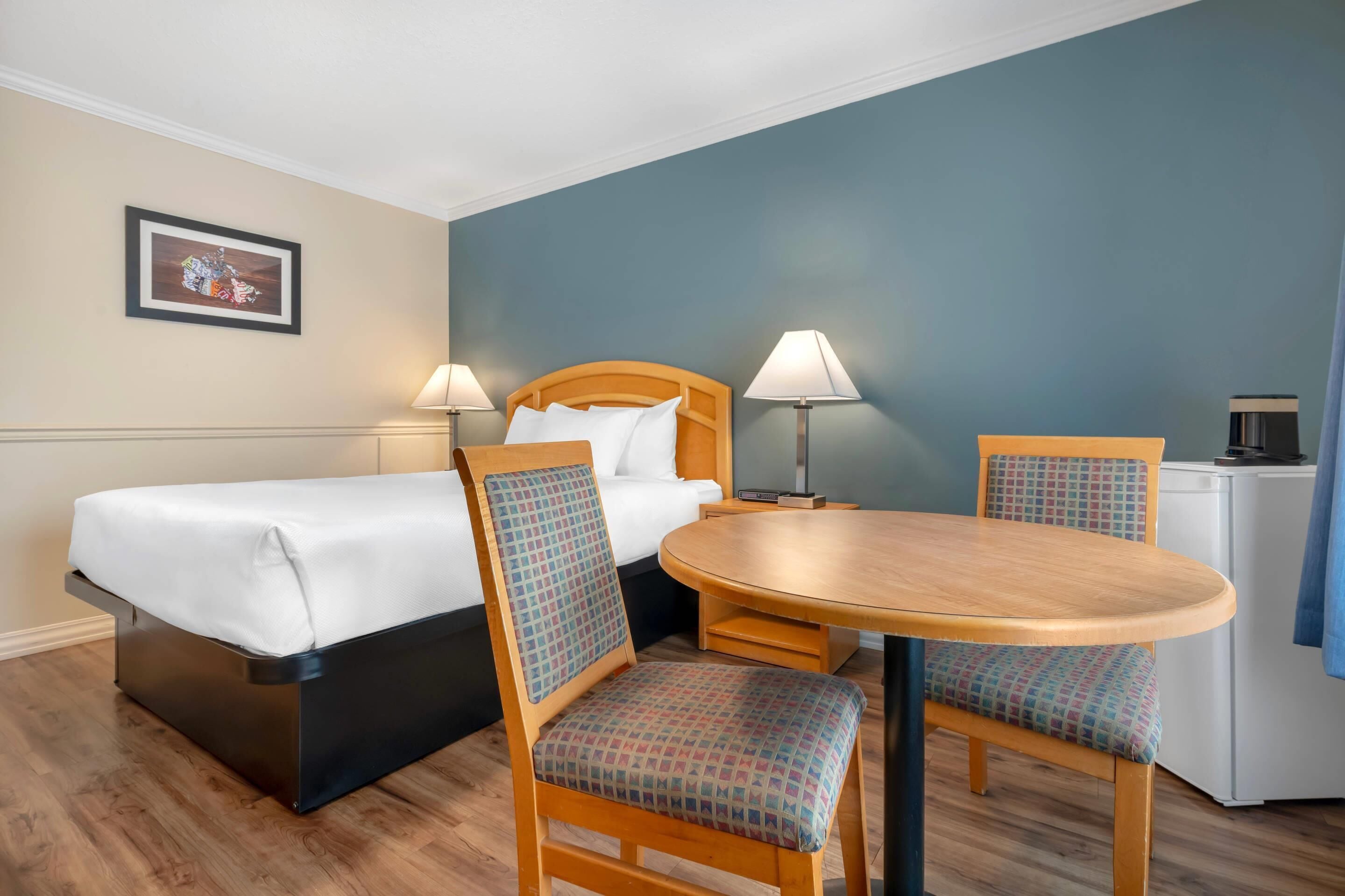 A hotel room with a bed, two chairs, a table, and a small kitchenette.