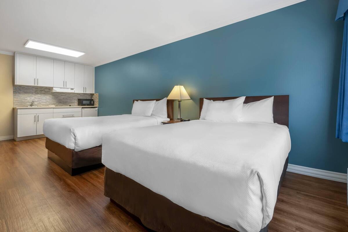 A hotel room with two beds, a kitchenette, and a blue accent wall.