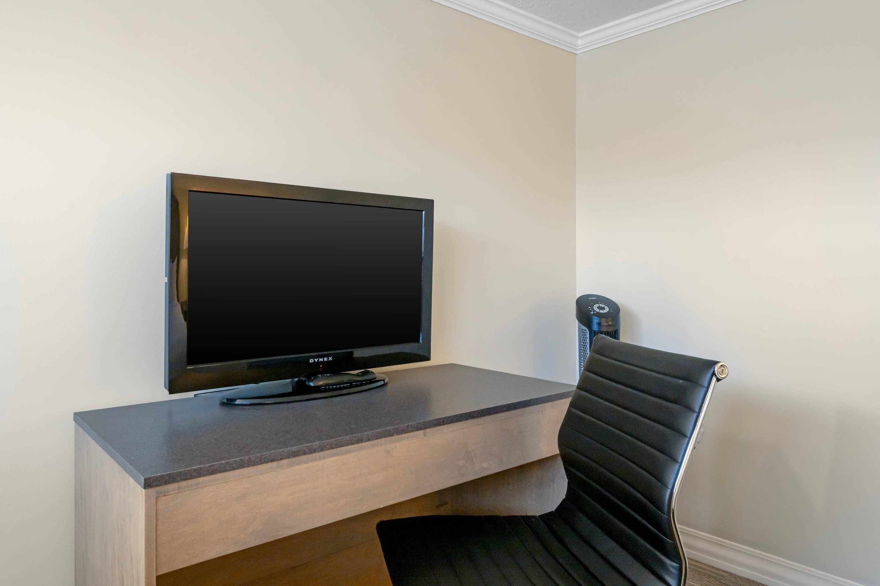 Un televisor de pantalla plana sobre un escritorio de madera, una silla negra y un purificador de aire fijado a la pared.