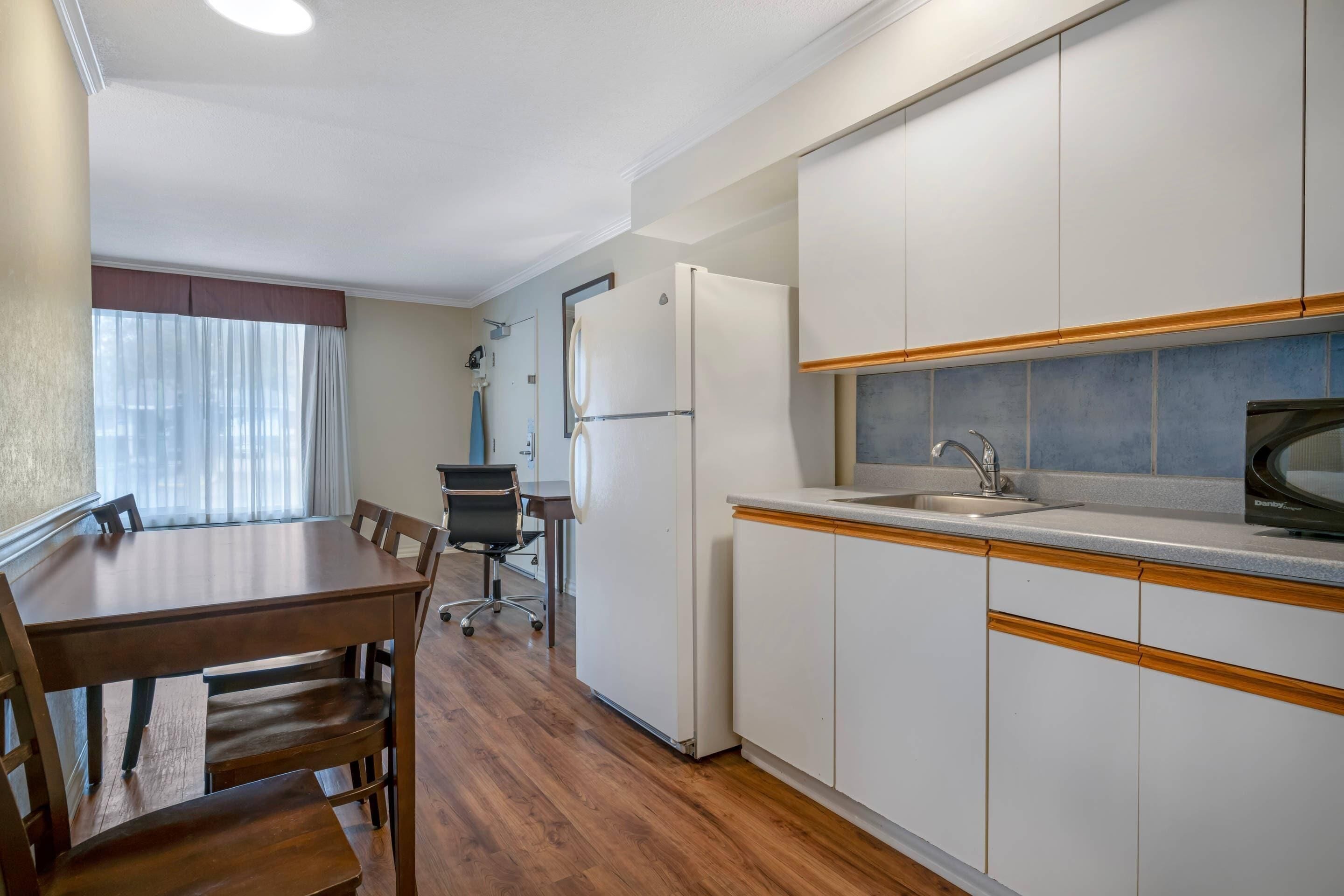 Una cucina funzionale con frigorifero, lavello e microonde. È presente un tavolo da pranzo con sedie e un piccolo angolo studio con scrivania e sedia.