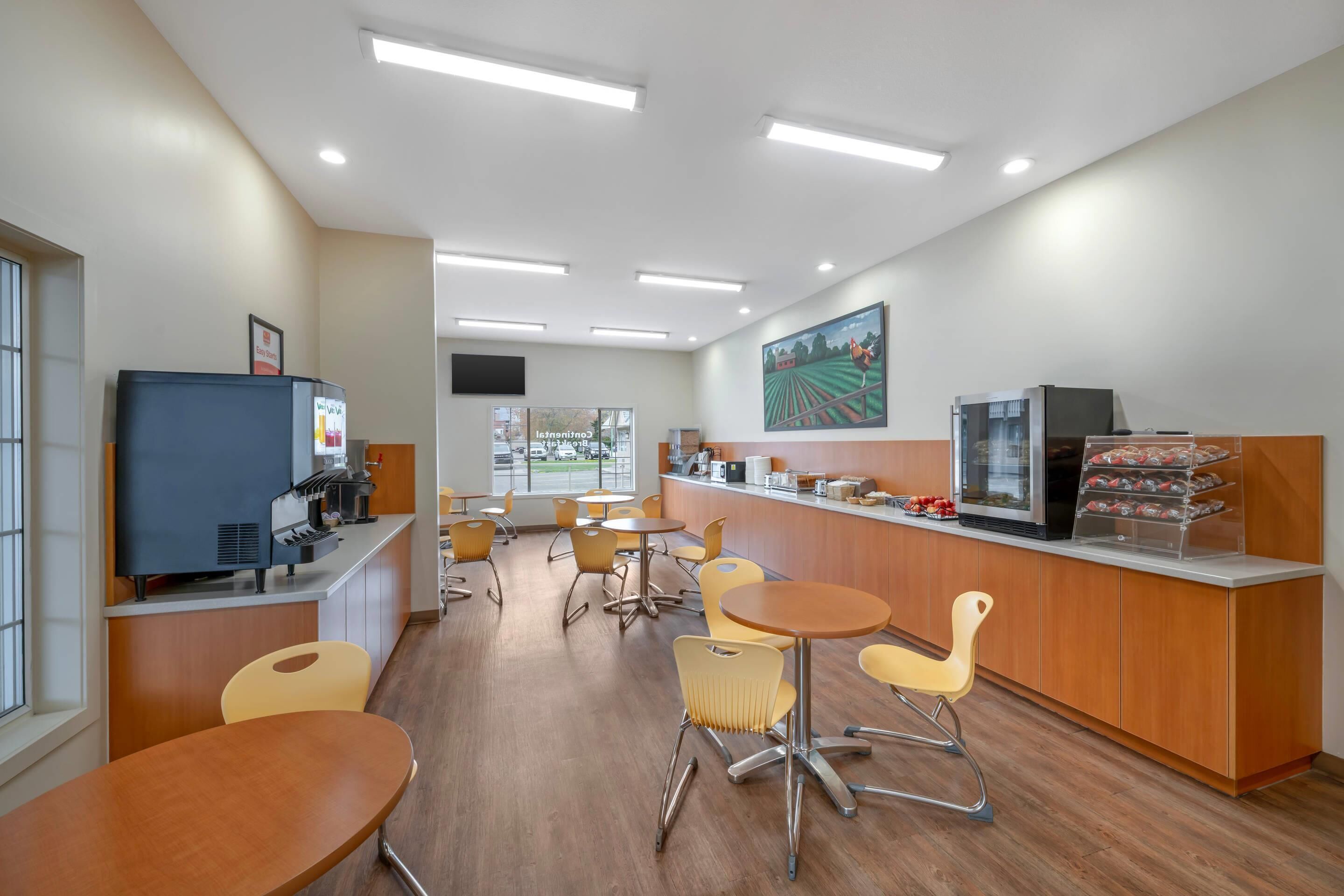 A modern cafe with wooden tables and chairs, a counter with a coffee machine, and a large painting on the wall.