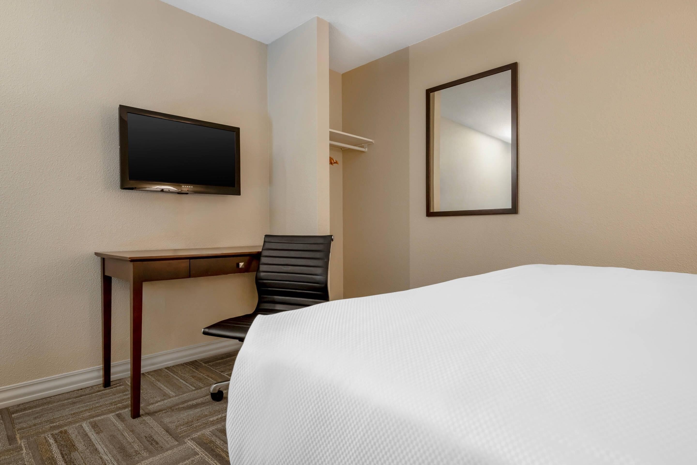 A hotel room with a bed, a desk, a chair, a TV, and a mirror.