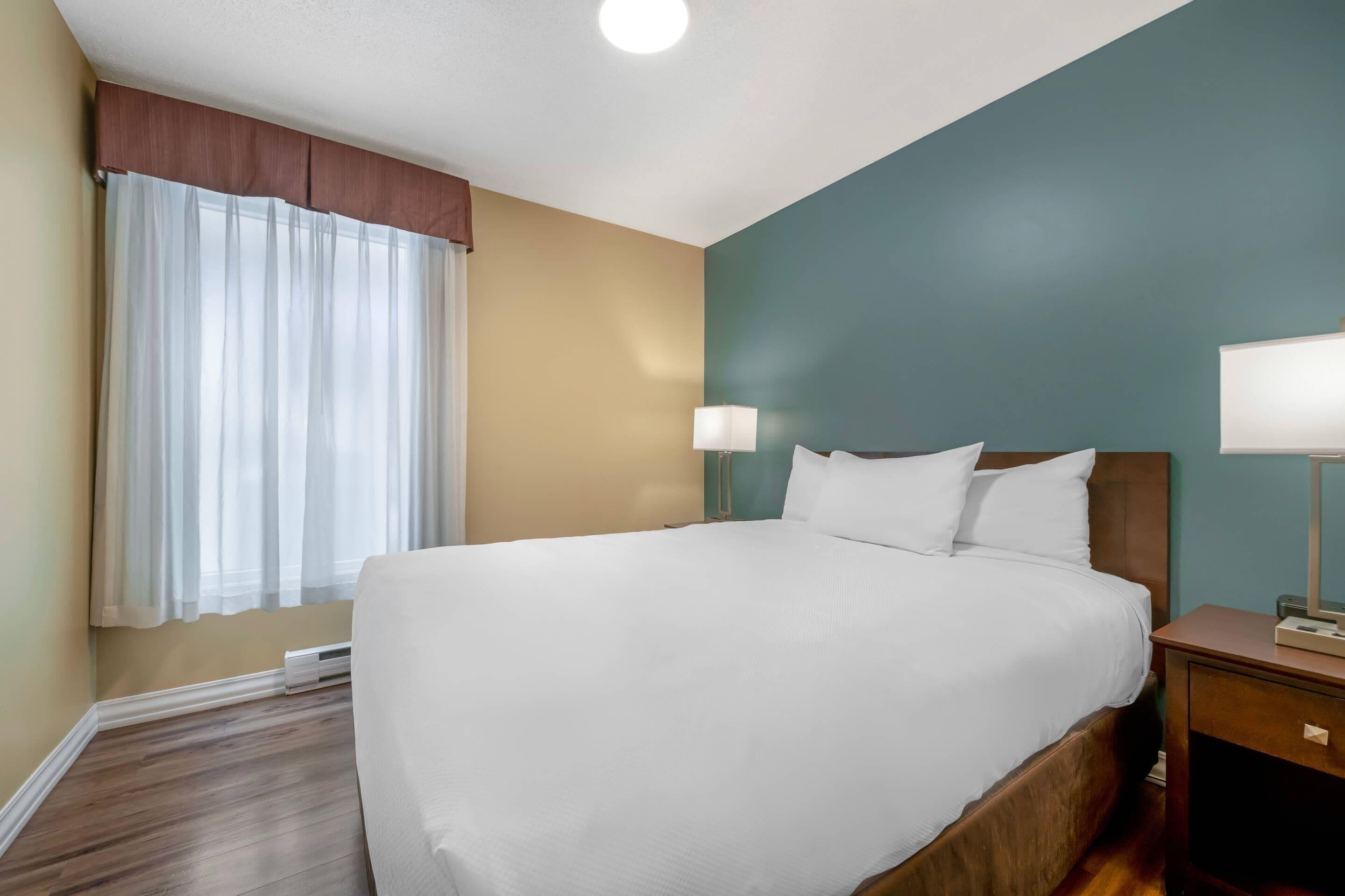 A hotel room with a large bed, bedside lamps, a window with curtains, and a wooden floor.